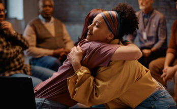 Group therapy participants hugging during mental health counseling at communicating center.