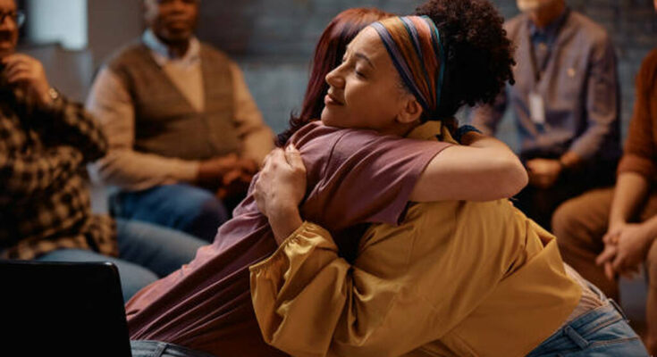 Group therapy participants hugging during mental health counseling at communicating center.